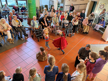 Eine Gruppe Senioren und Seniorinnen sitzt in der Aula des Kreis-Seniorenwohnheims und sieht den Kindern beim St. Martin-Schauspiel zu. 