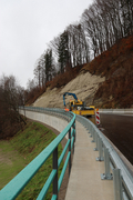 Ein Baufahrzeug steht am Straßenrand der neuen Straße. Daneben sind die Stützwand und Schutzeinrichtungen zu sehen. 