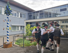 Vier Männer in Tracht tanzen neben dem Maibaum.