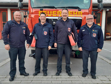 Vier Männer stehen in Feuerwehr-Uniform vor einem Feuerwehrauto.