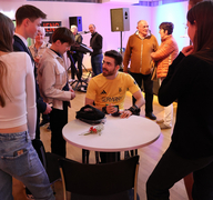 Moritz Brückner sitzt im Rollstuhl an einem Tisch. Mehrere junge Sportler umringen ihn. 